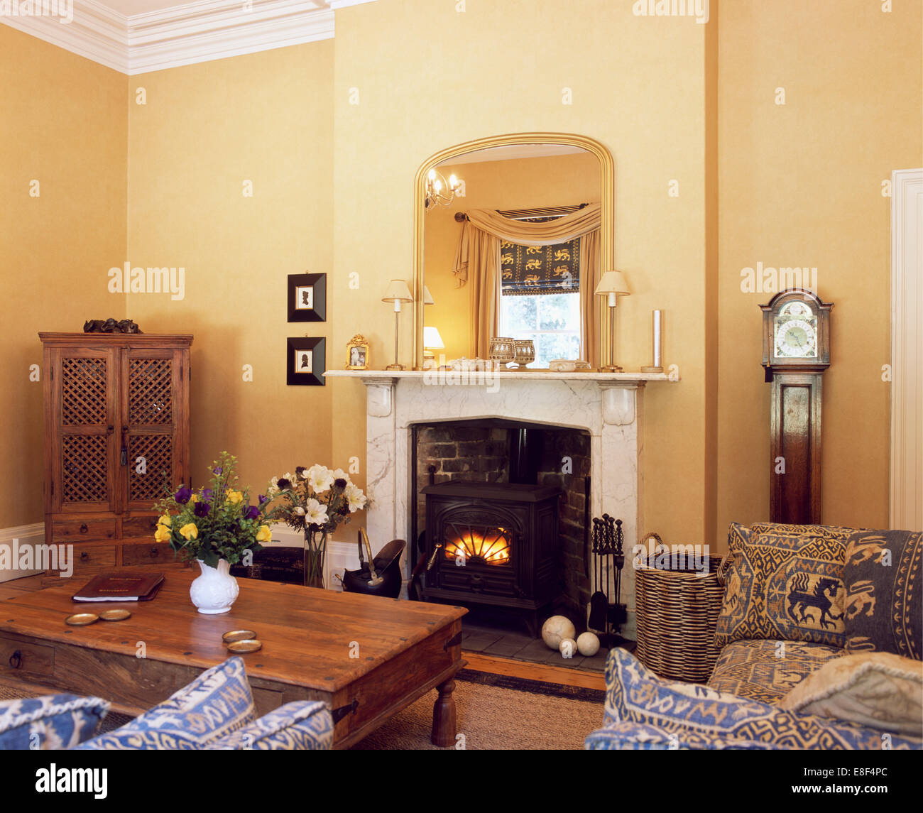 Miroir doré au-dessus de cheminée en marbre avec poêle à bois dans le pays de séjour avec table à café en bois indonésien Banque D'Images