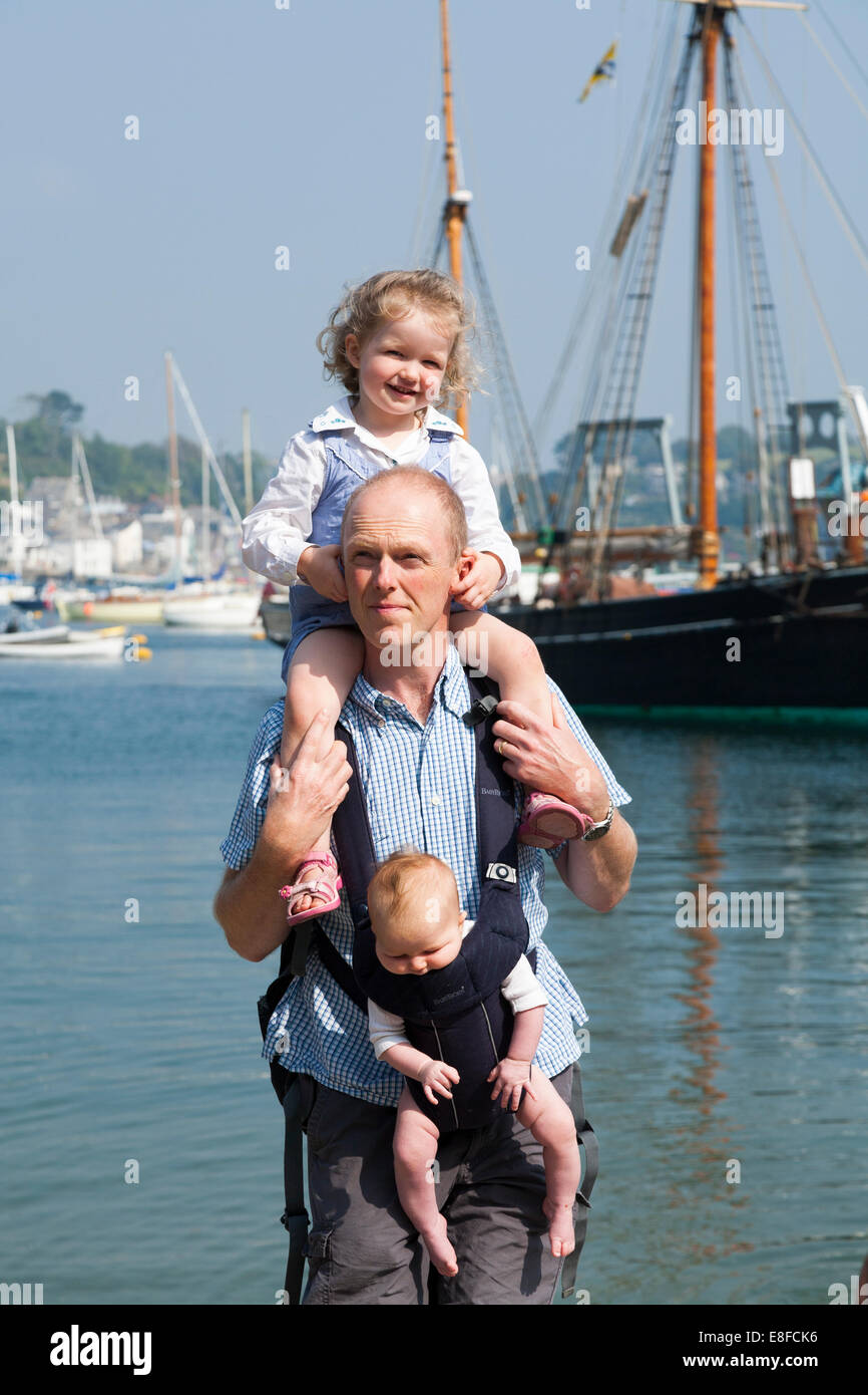 Papa mature / père avec 2 / 2 enfants ; un enfant sur les épaules et le bébé en écharpe. Cornwall UK. Banque D'Images