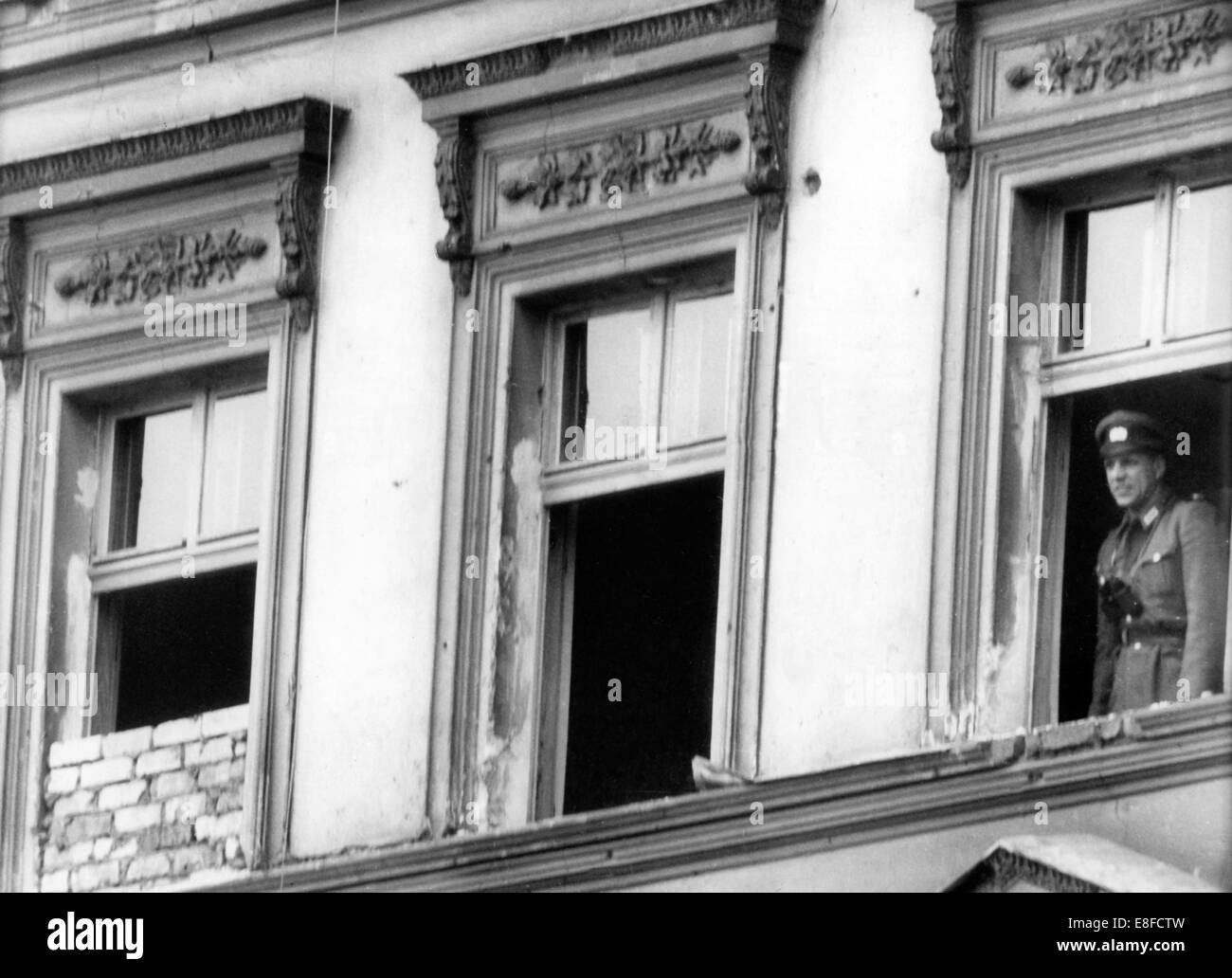 Un homme de la police de la police a un regard par une fenêtre d'une maison à la frontière, qui n'a pas encore été murés, le 1er octobre en 1961 dans la rue Bernauer à Berlin. Banque D'Images