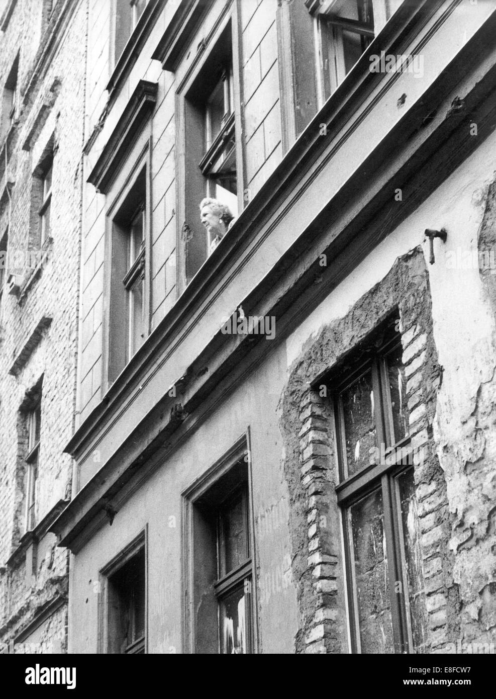 Une femme a un regard par la fenêtre d'une maison à la frontière, qui appartient à l'Est de Berlin, à l'ouest de la ville le 24 août en 1961, qui commence juste en face de la maison. Les fenêtres dans les étages inférieurs ont été murés. Banque D'Images