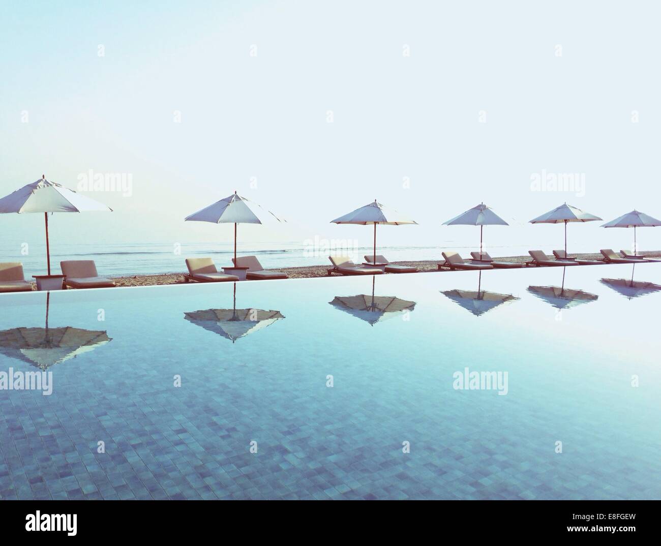 Des parasols sont reflétées dans une piscine avec plage derrière Banque D'Images