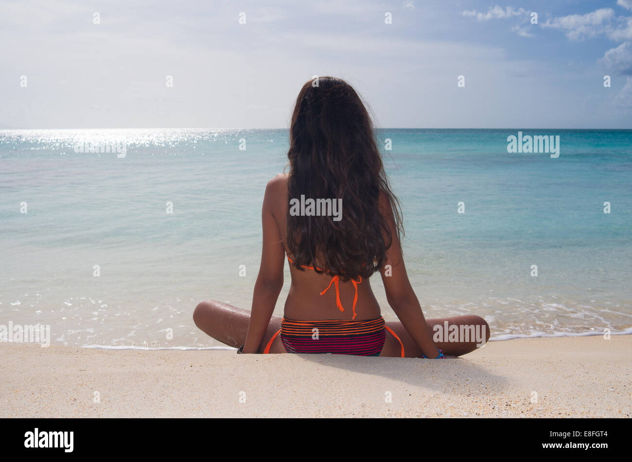Vue arrière du girl sitting on plage de Darkwood, Antigua, Antilles Banque D'Images