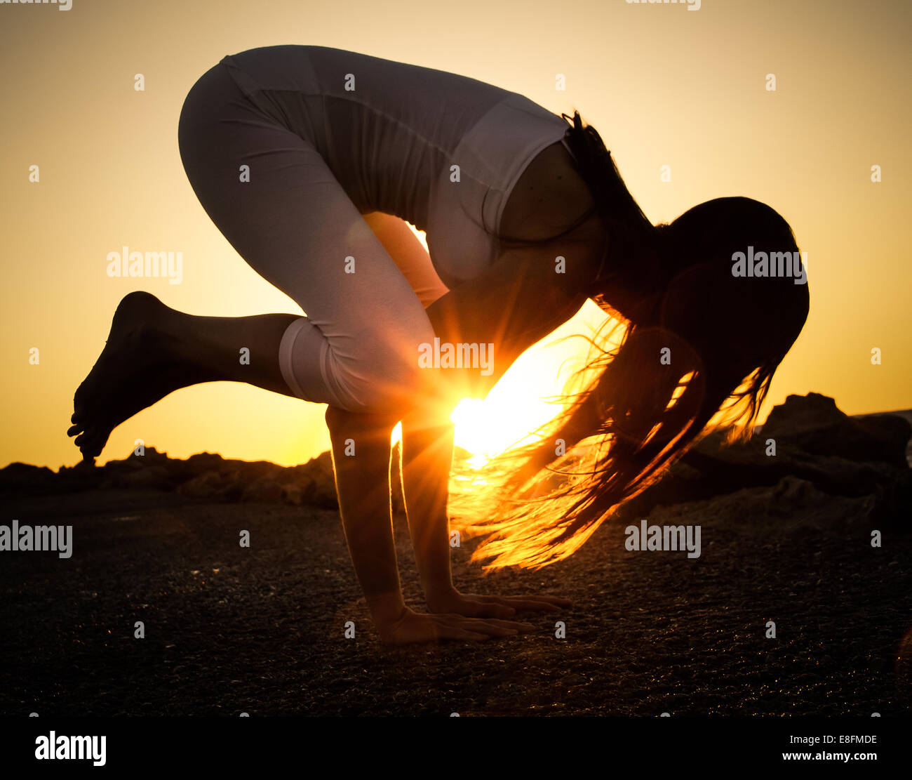 Woman practicing yoga on beach at sunset Banque D'Images
