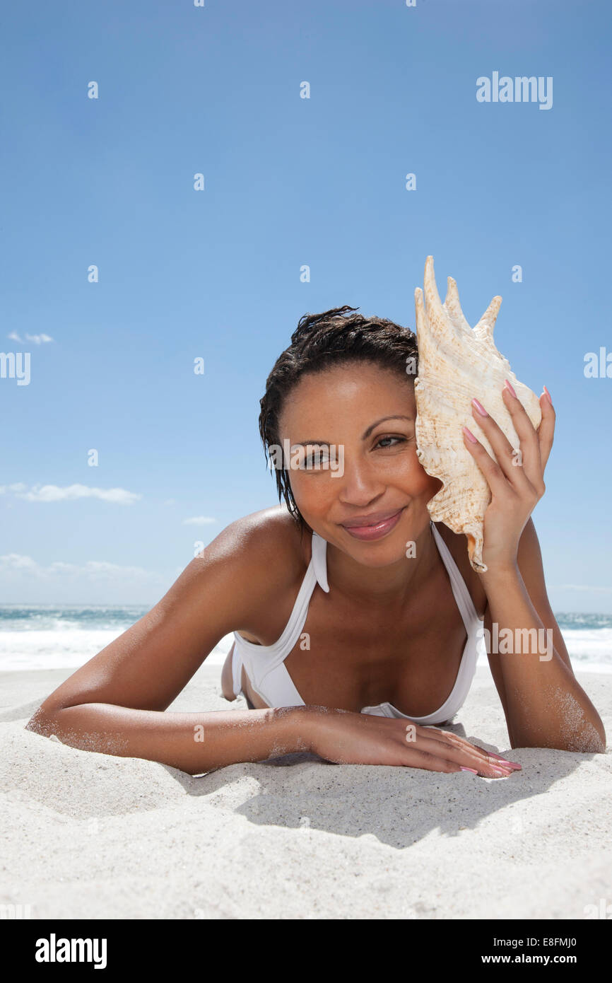 Femme couché sur la plage à l'écoute d'un conch Shell, Cape Town, Western Cape, Afrique du Sud Banque D'Images