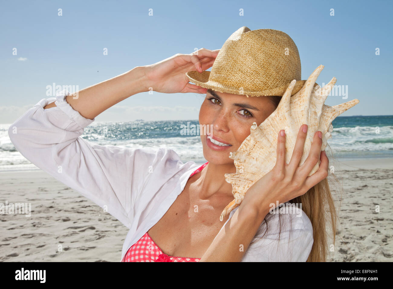 Jeune femme à l'écoute de conch Shell sur la plage, le Cap, le Cap occidental, Afrique du Sud Banque D'Images