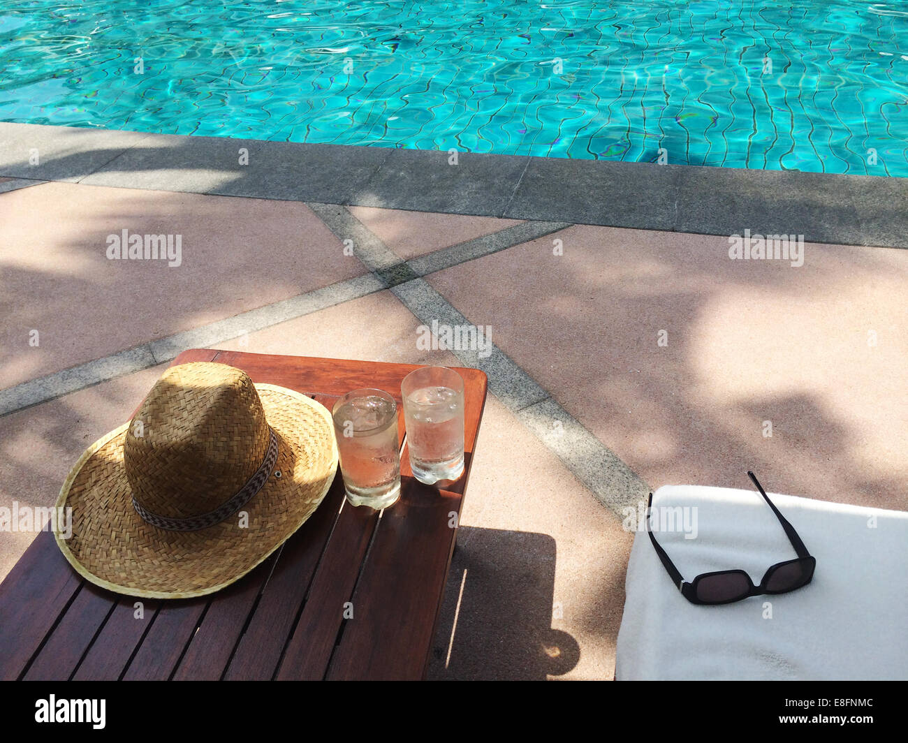 Chapeau, lunettes de soleil de paille et deux verres d'eau par piscine Banque D'Images