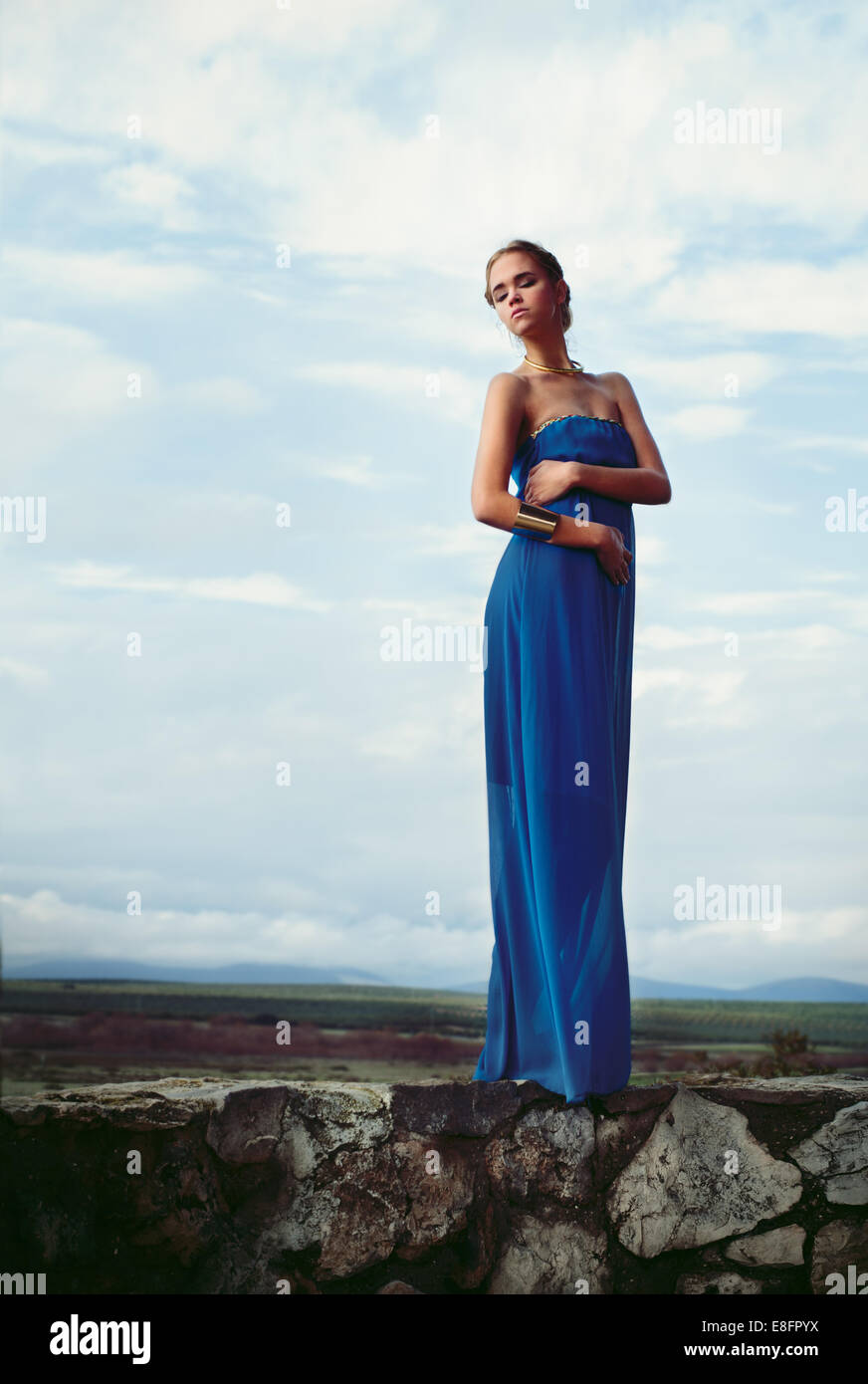Femme portant robe bleu debout sur mur de pierre Banque D'Images