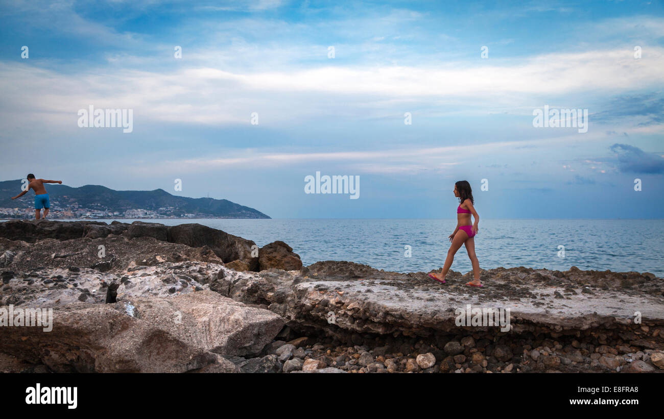 Deux enfants à marcher le long de la plage rocheuse, Barcelone, Espagne Banque D'Images