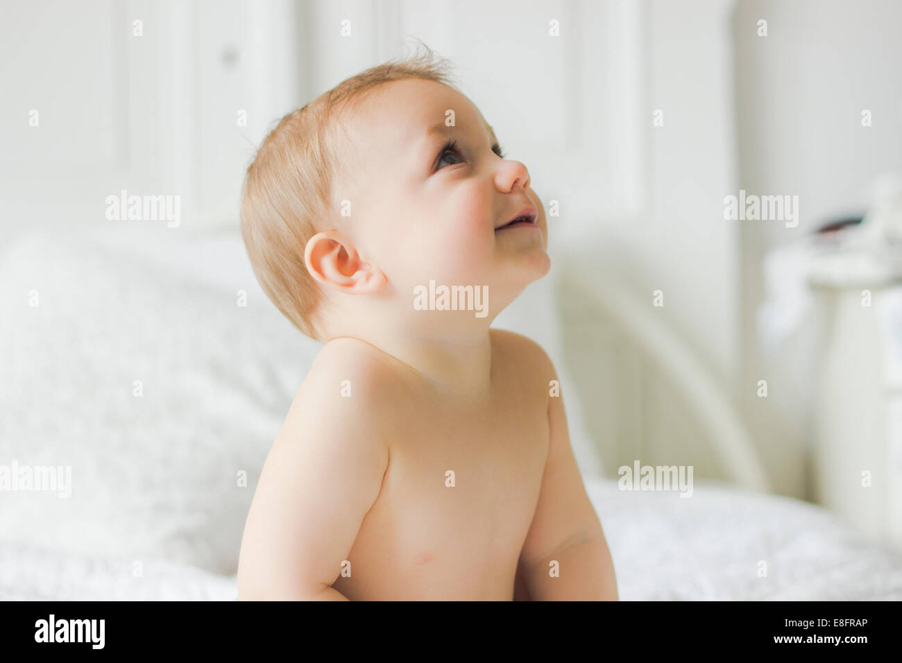 Portrait of Smiling baby sitting on lit dans la chambre Banque D'Images