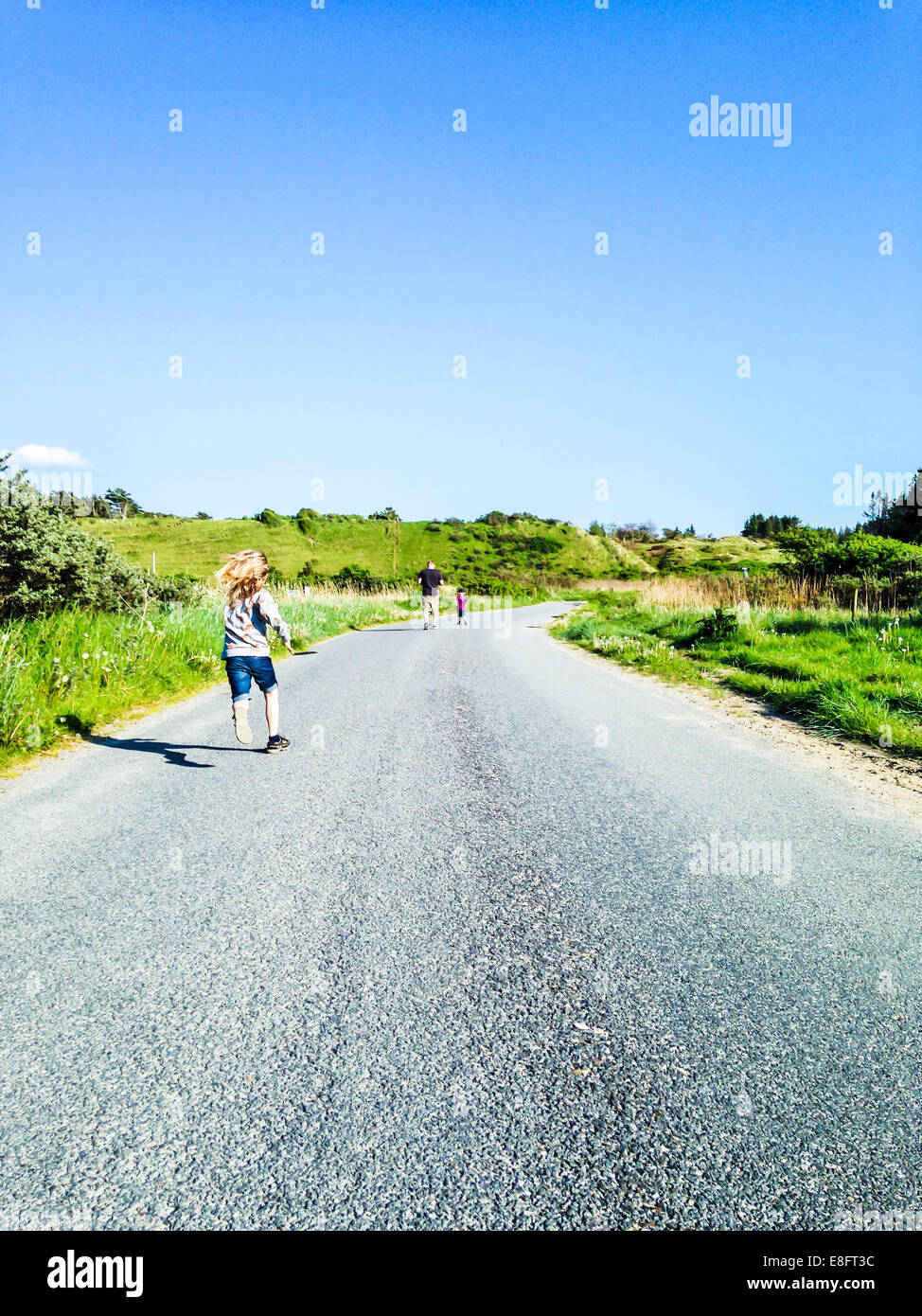 Vue arrière de l'homme couler sur route avec deux fils, Danemark Banque D'Images