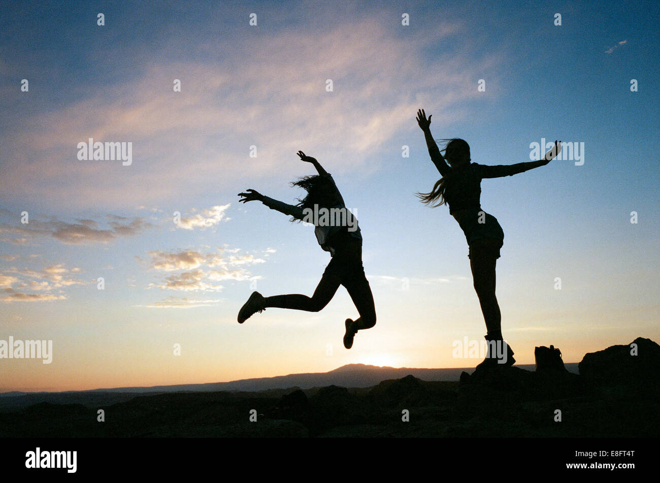 Silhouettes de deux femmes sautant dans l'air au coucher du soleil Banque D'Images