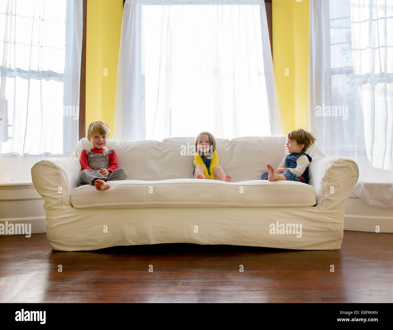 Trois enfants s'assoyant sur un canapé dans le salon Banque D'Images