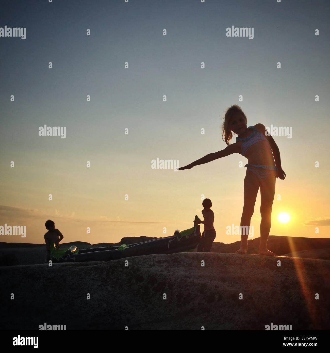 Silhouette de trois enfants avec un kayak à rock au coucher du soleil, la Norvège Banque D'Images