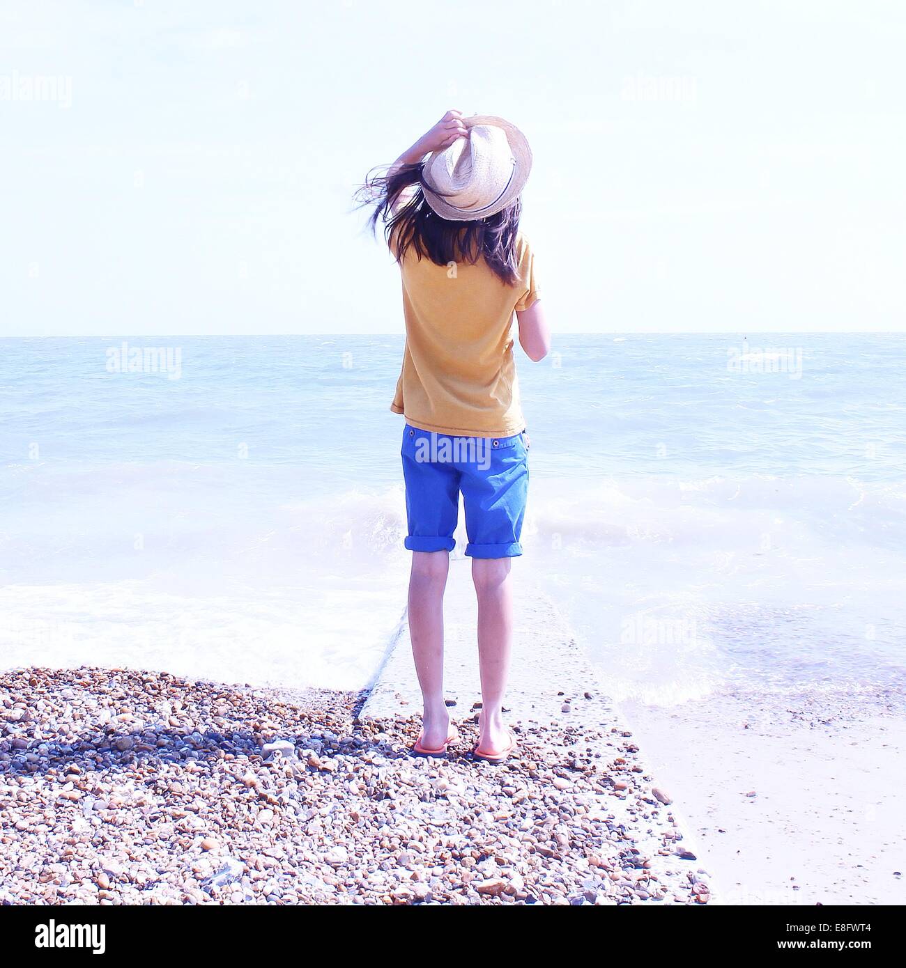 Vue arrière du Girl standing on beach holding hat Banque D'Images