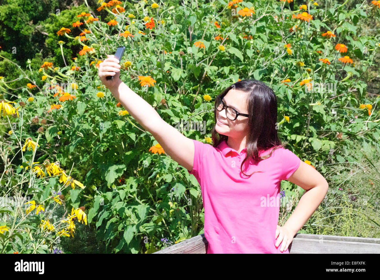 Girl (10-11) en tenant contre bush floraison selfies Banque D'Images