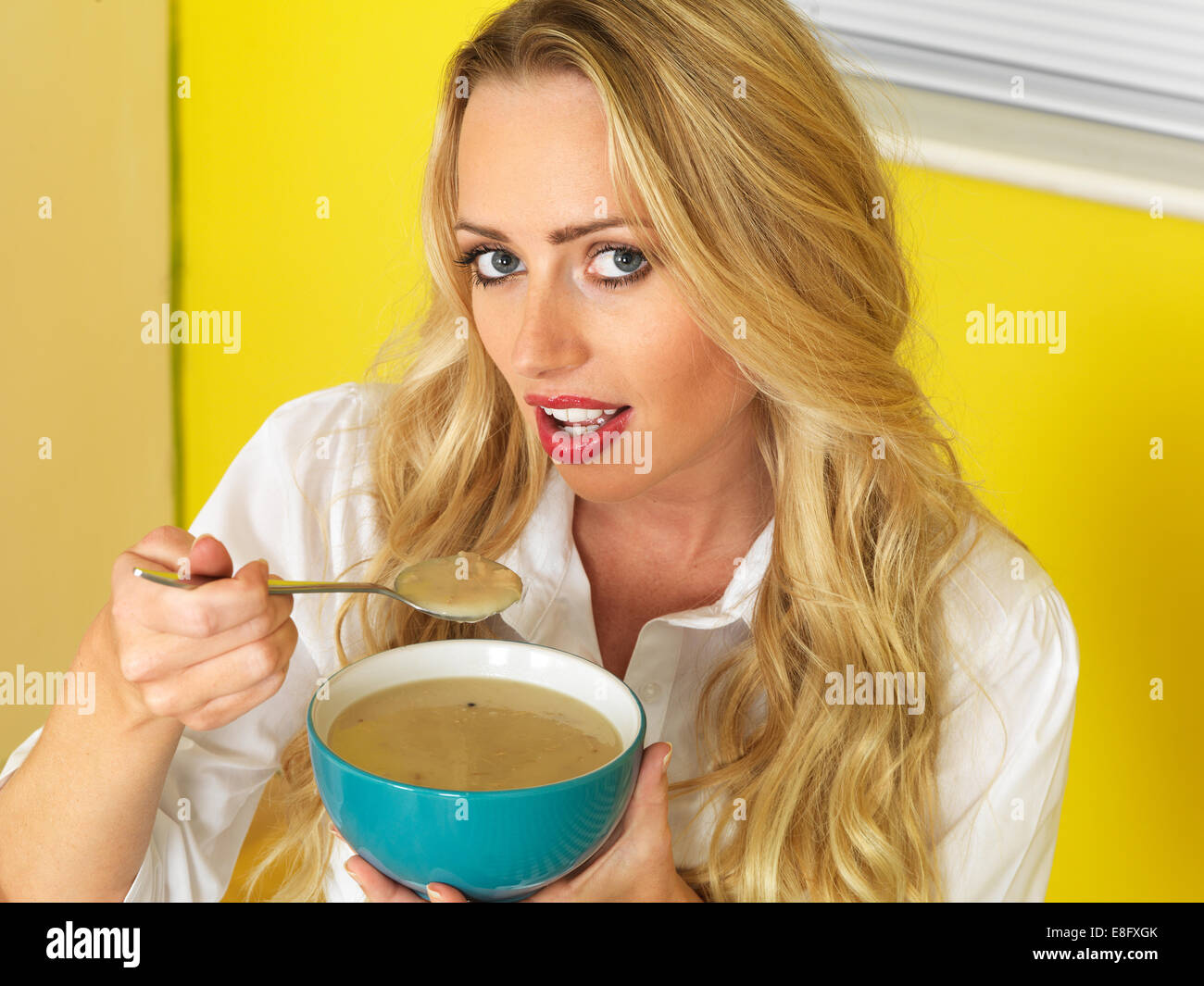 Confident Happy Young Woman, manger un bol de soupe nourrissante chaude, sur fond jaune Banque D'Images