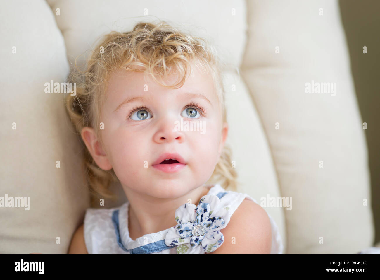 Adorable blonde aux yeux bleus et aux cheveux Petite fille assise dans la chaise. Banque D'Images