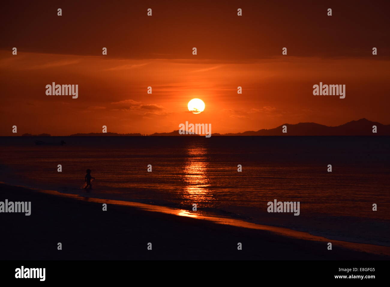 Dernière Lumière, enfant jouant au bord de l'eau tandis que les couchers de soleil. Coucher de soleil rouge, rouge ciel, Fidji Banque D'Images