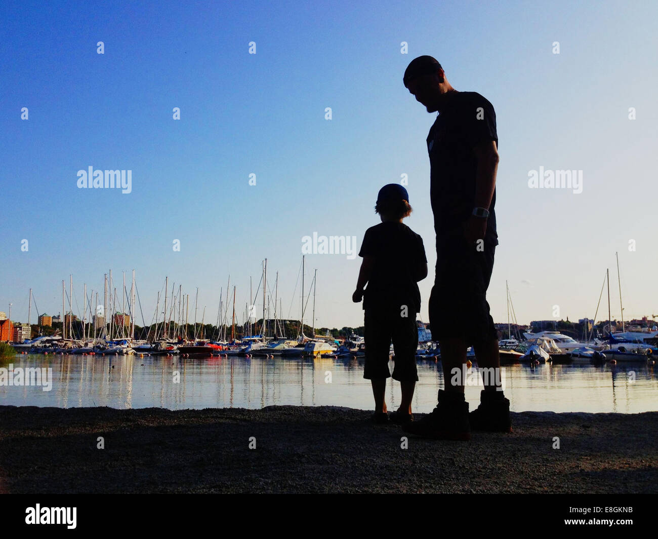Stockholm, Suède, un garçon et son père de lancer des pierres dans l'eau et regarder les bateaux Banque D'Images