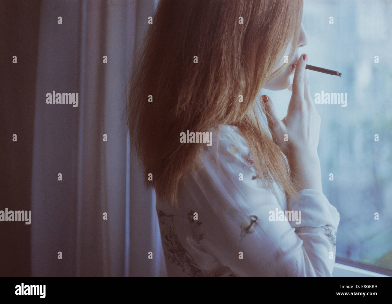 Portrait d'une femme debout par fenêtre fumeur Banque D'Images