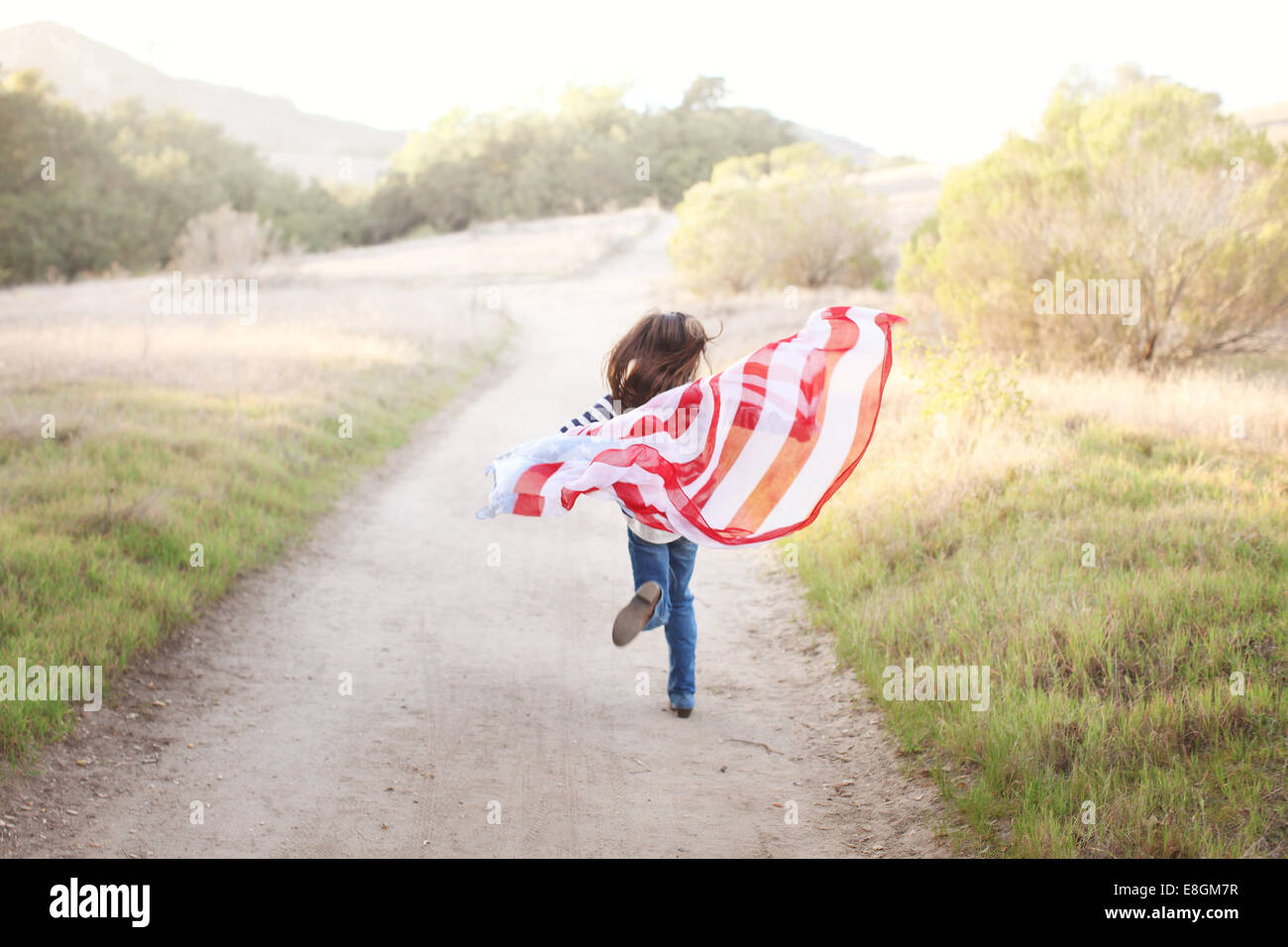 Vue arrière de Girl courir le long d'un sentier tenant un drapeau américain, USA Banque D'Images