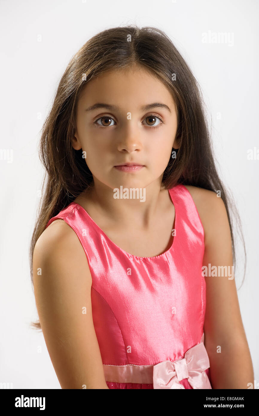 Jolie petite fille dans une élégante robe rose et une écharpe regardant la caméra avec une expression solennelle et de grands yeux noirs, sur fond blanc Banque D'Images