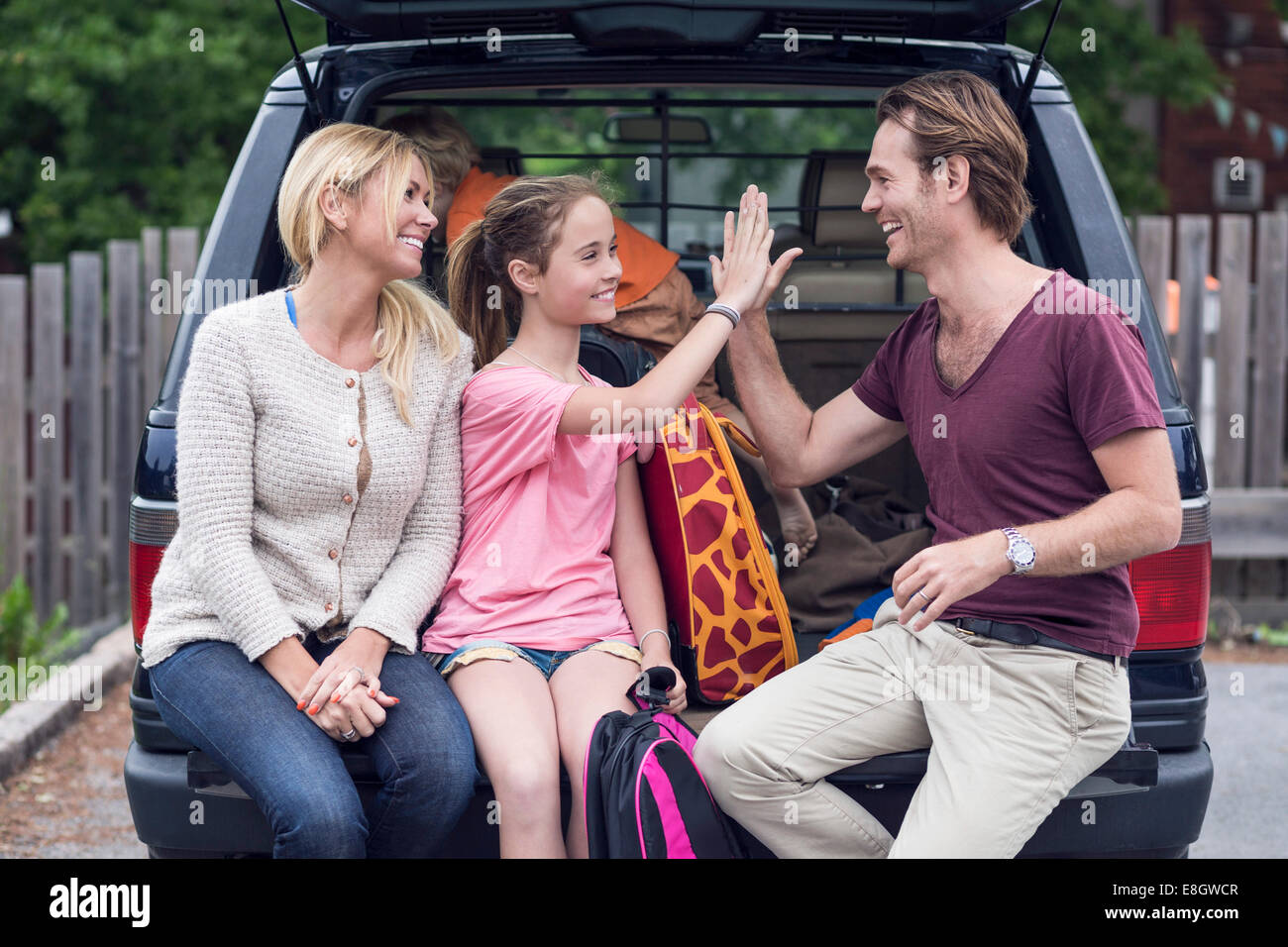 Smiling woman looking at père et fille haute donnant cinq dans coffre de voiture Banque D'Images