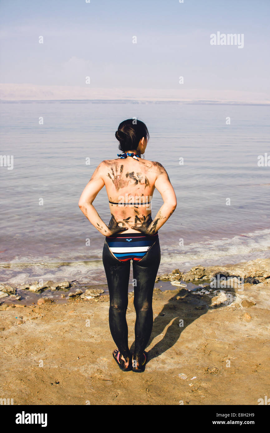 La Jordanie, femme japonaise avec boue de la mer morte sur le bas de son corps à une plage sur la côte jordanienne de la mer Morte Banque D'Images