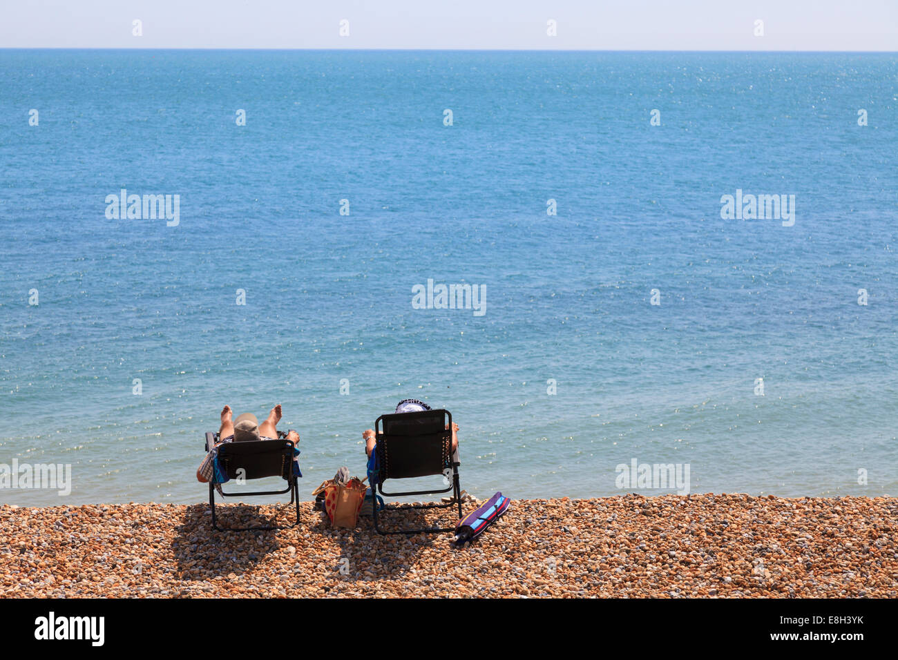 Deux personnes dans des chaises longues sur la plage de galets par mer de l'arrière. Banque D'Images