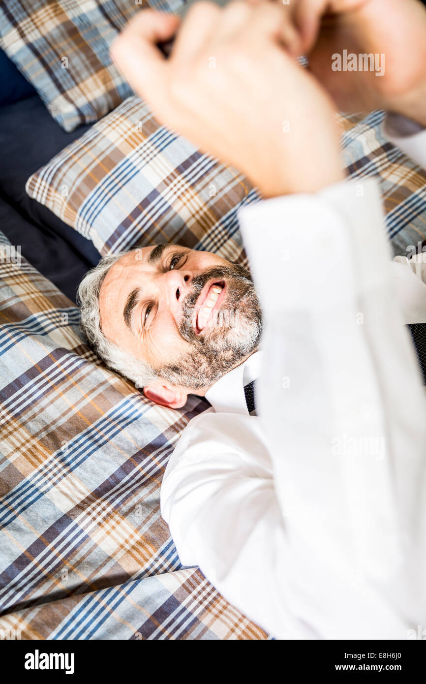 Portrait of happy businessman étendu sur son lit en regardant son smartphone Banque D'Images