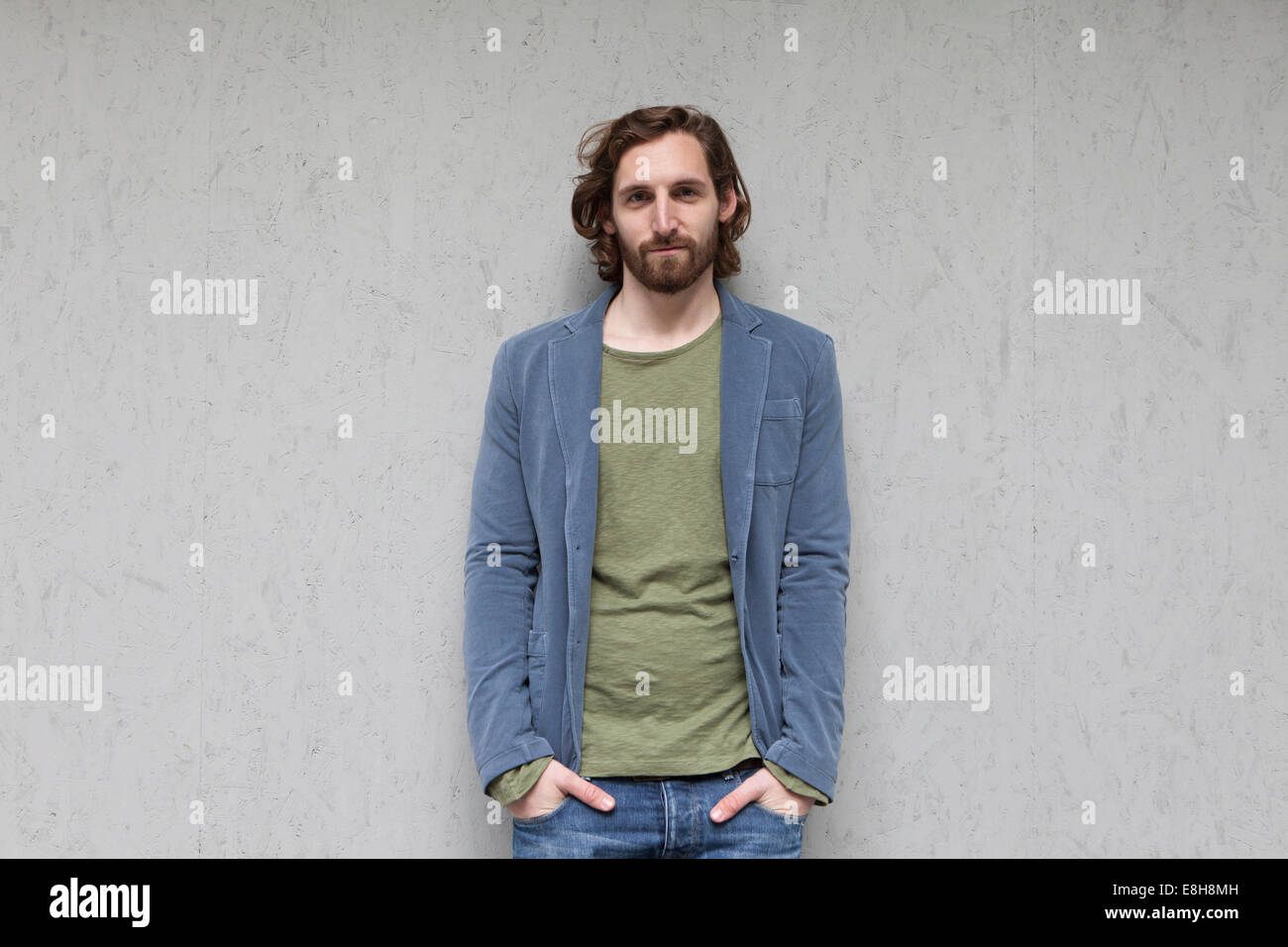 Portrait of smiling young man leaning contre un mur gris Banque D'Images