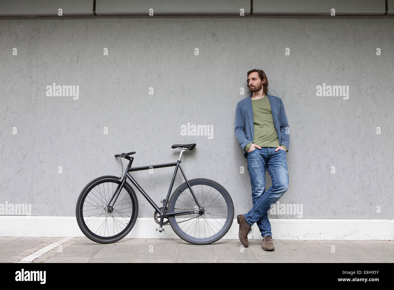 Germany, Bavaria, Munich, young man standing outre son cycle de course s'appuyant sur un mur Banque D'Images