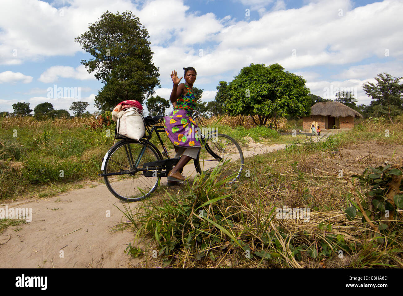 Femme sur un vélo dans un milieu rural village zambien bonjour vagues. Banque D'Images