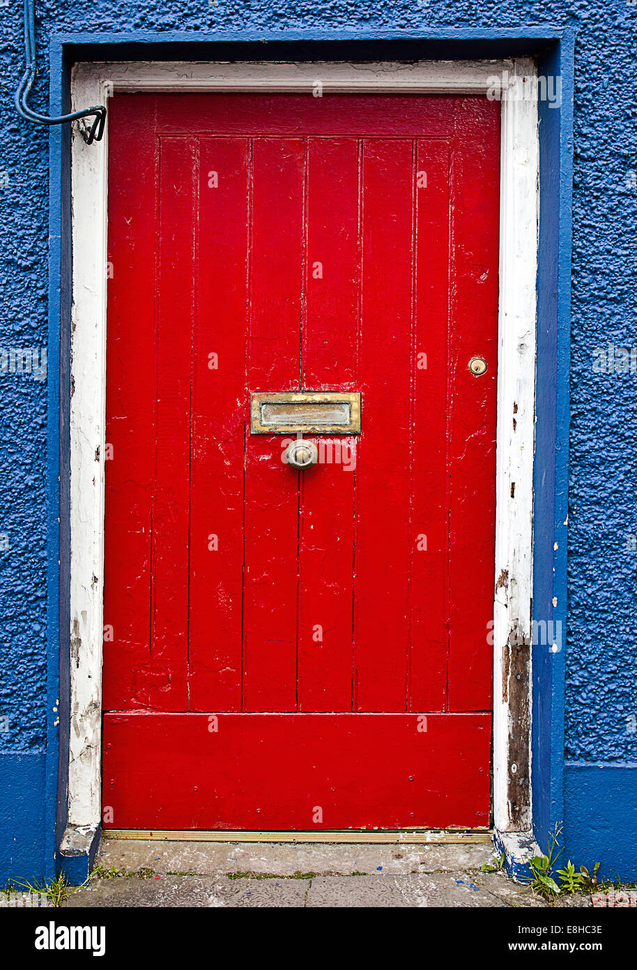 Une porte en bois peint rouge avec lettre laiton fort et le bouton bleu entouré d'un mur en pointillés à des cailloux à Dingle Comté de Kerry Banque D'Images