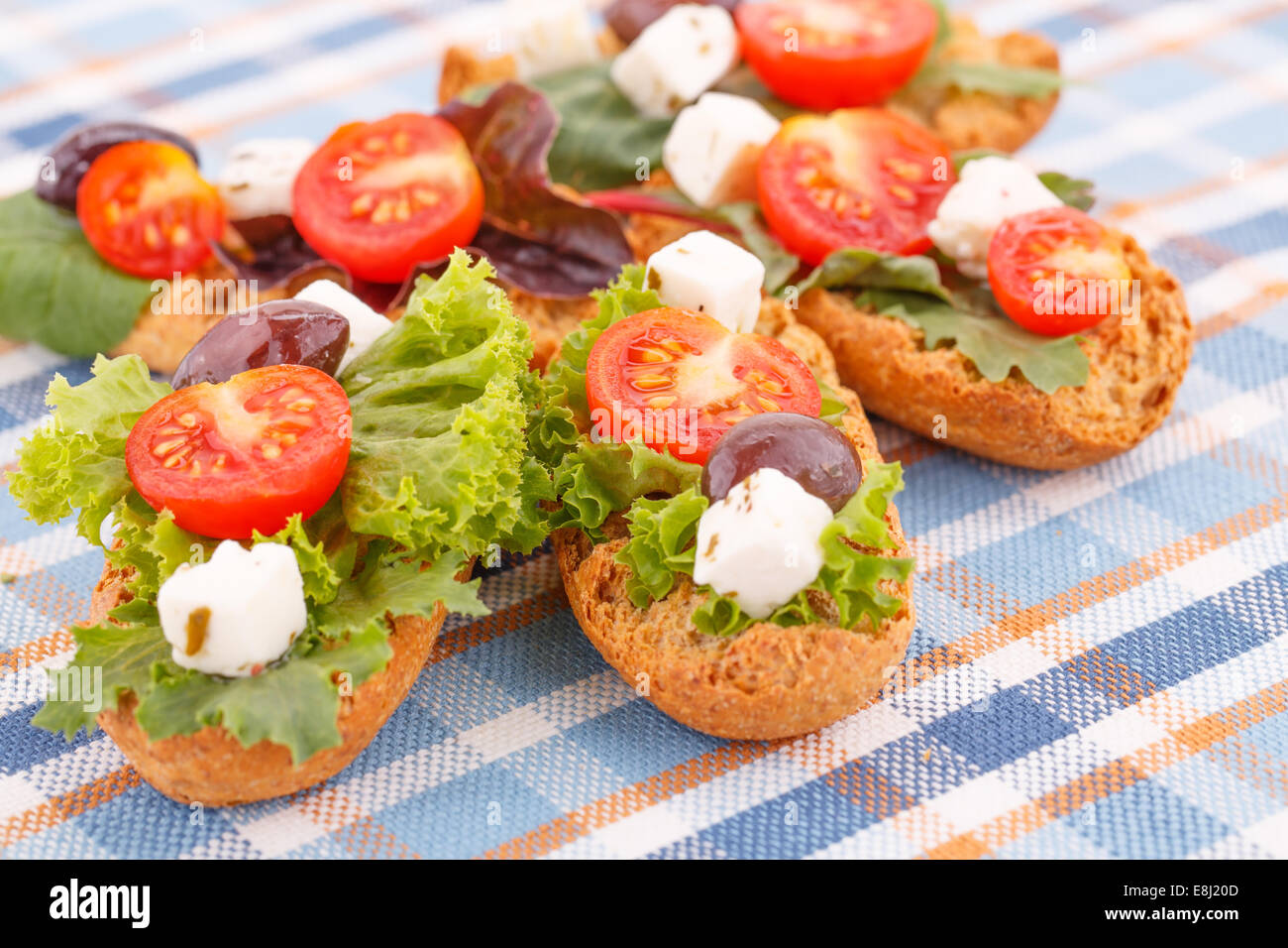 Des sandwichs avec des biscottes, légumes, olives et fromage feta sur nappe colorée. Banque D'Images