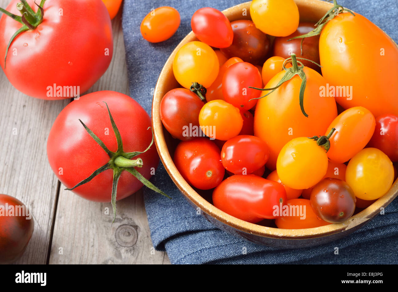 Différents types colorés des tomates dans un bol sur la table en bois. Rouge, jaune, grandes et petites tomates. Banque D'Images