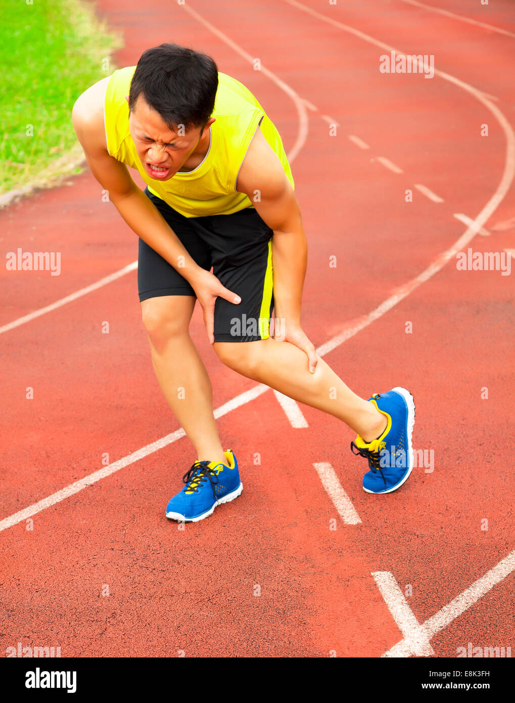 Young male runner souffrant de crampes de jambe sur la piste dans le stade Banque D'Images