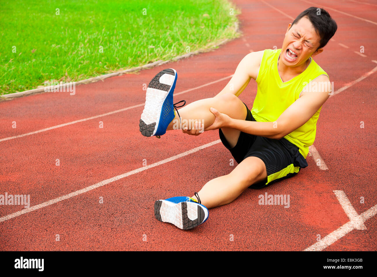 Young male runner souffrant de crampes de jambe sur la piste dans le stade Banque D'Images