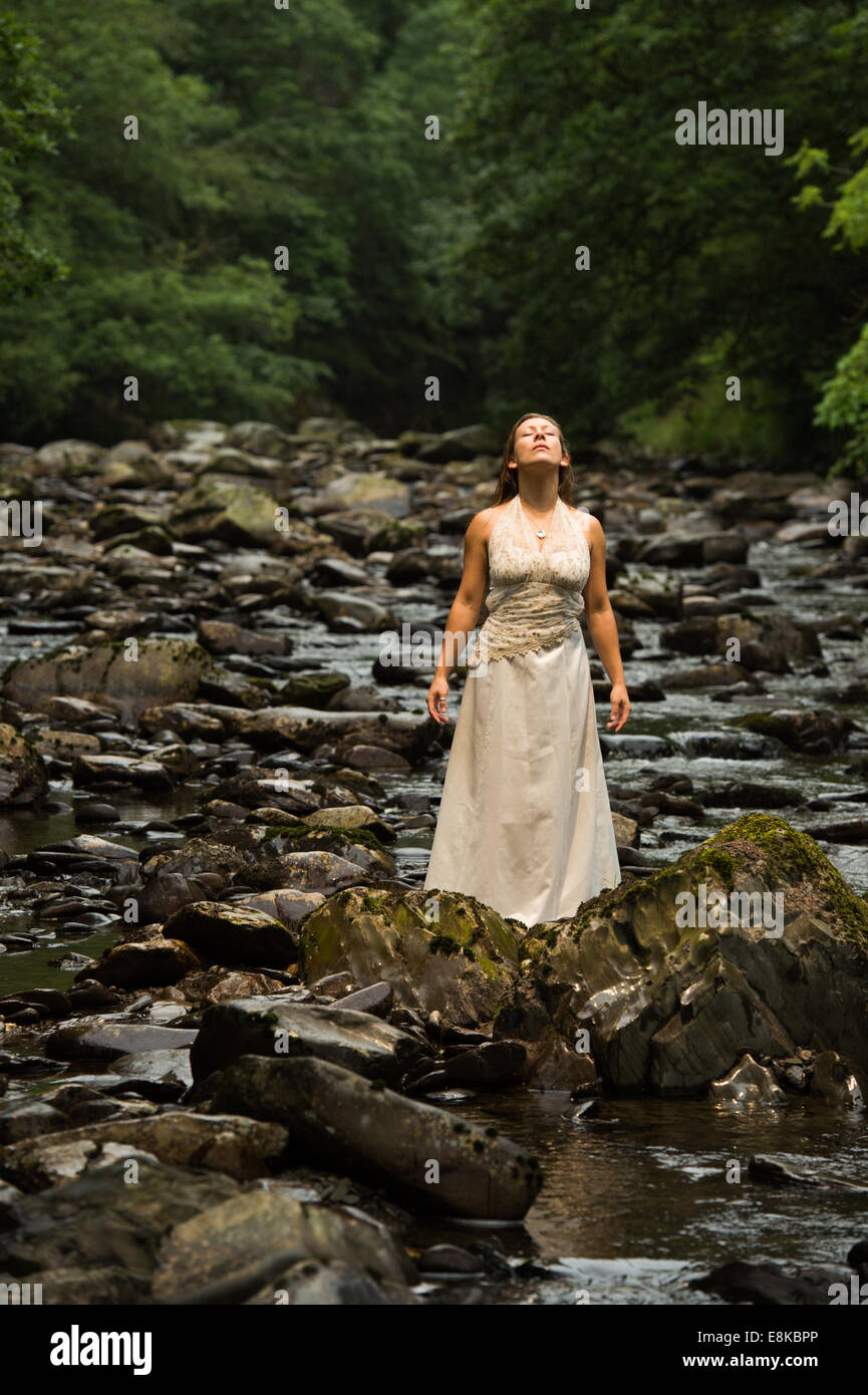 Corbeille la robe : un 'bride' de porter sa robe de mariage seul se tenant dans un rocher dans une rivière avec ses yeux fermés Banque D'Images