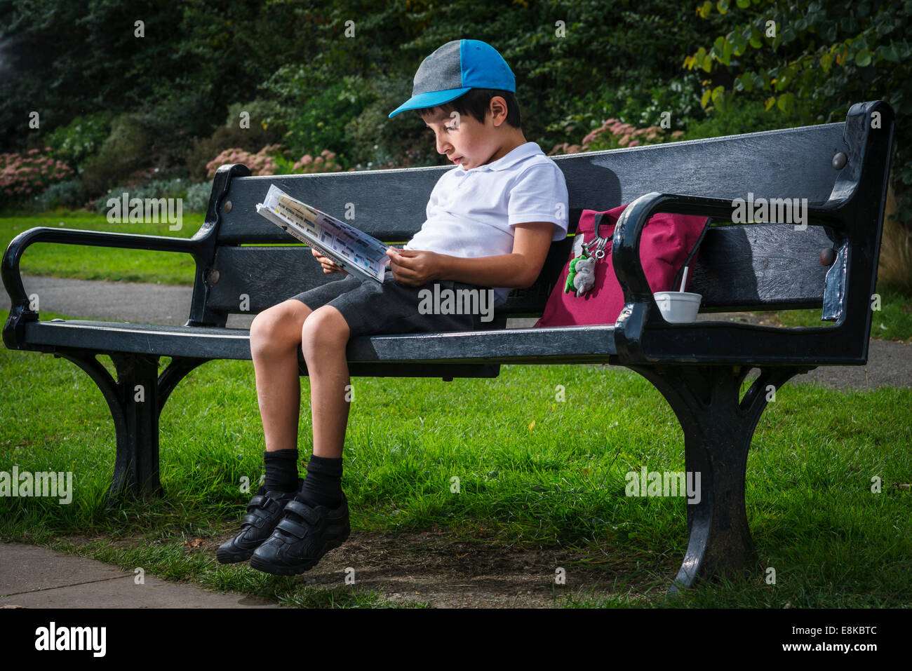 Écolier assis sur un banc de parc en lisant un livre Banque D'Images