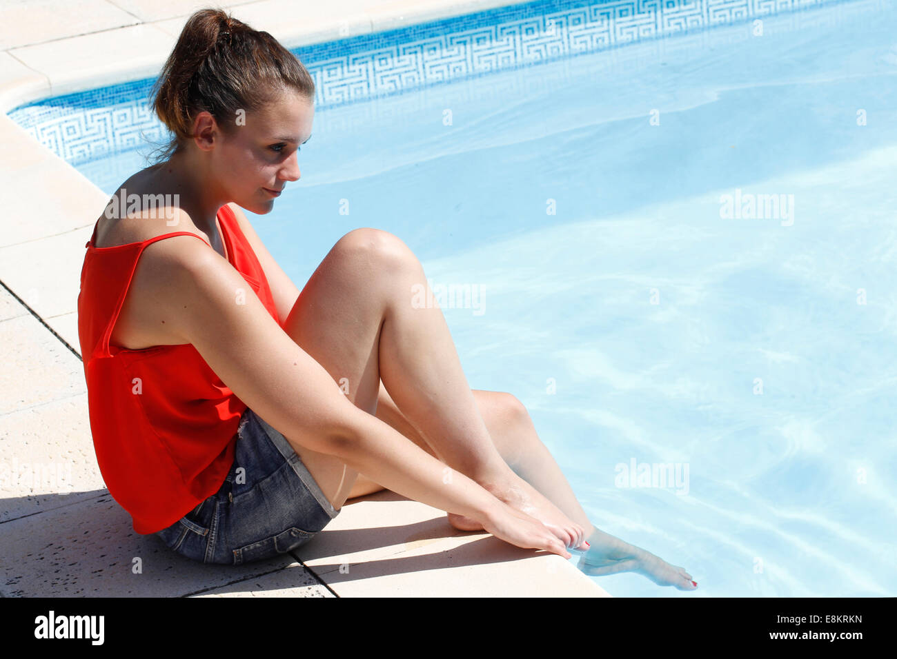 Une jeune femme assise sur le bord d'une piscine avec ses pieds dans l'eau. Banque D'Images