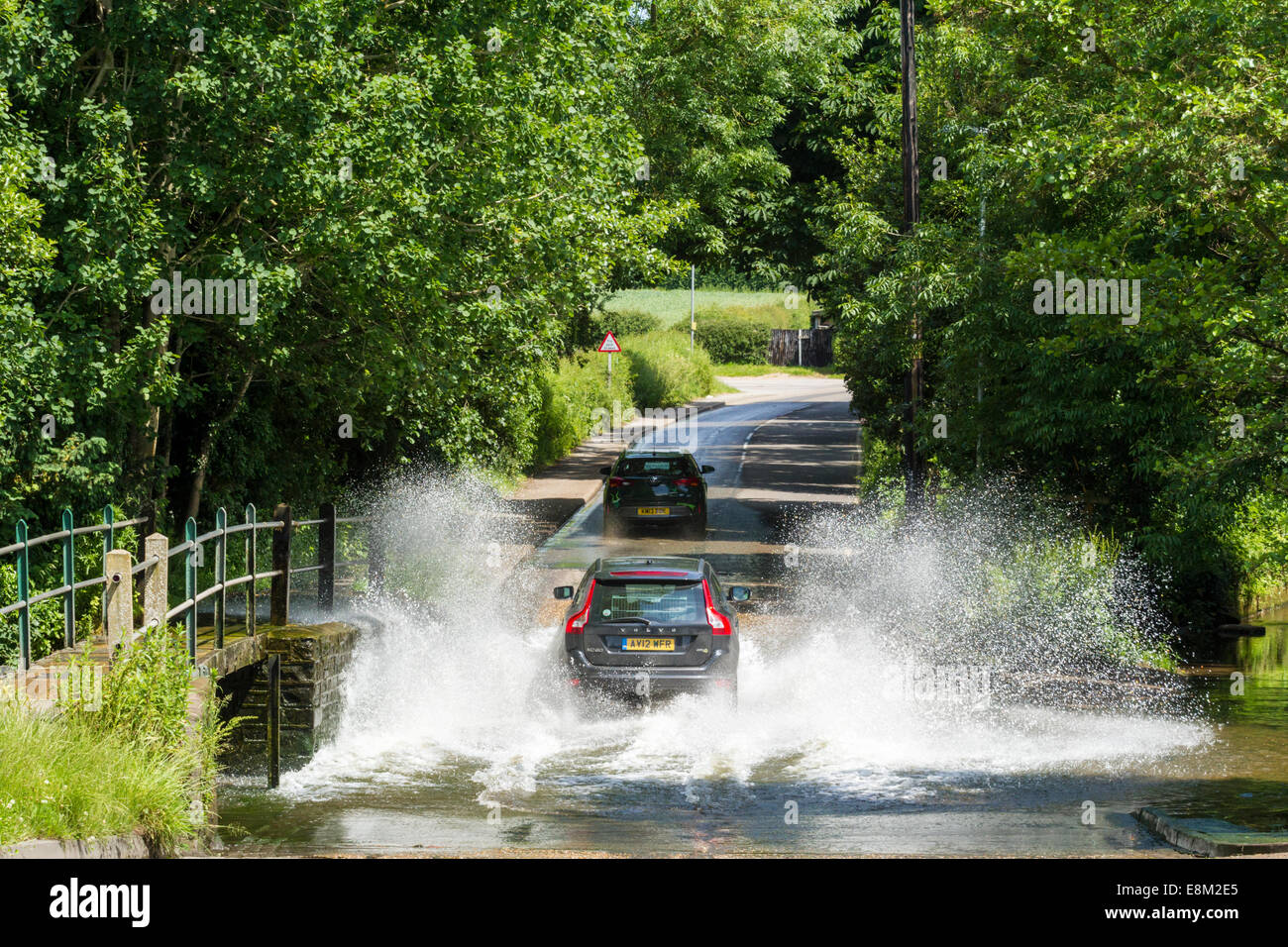 La conduite du véhicule par un ruisseau. Une voiture aux projections d'eau lorsque entraîné par la Ford de traverser la route à Rufford, Dorset, England, UK Banque D'Images