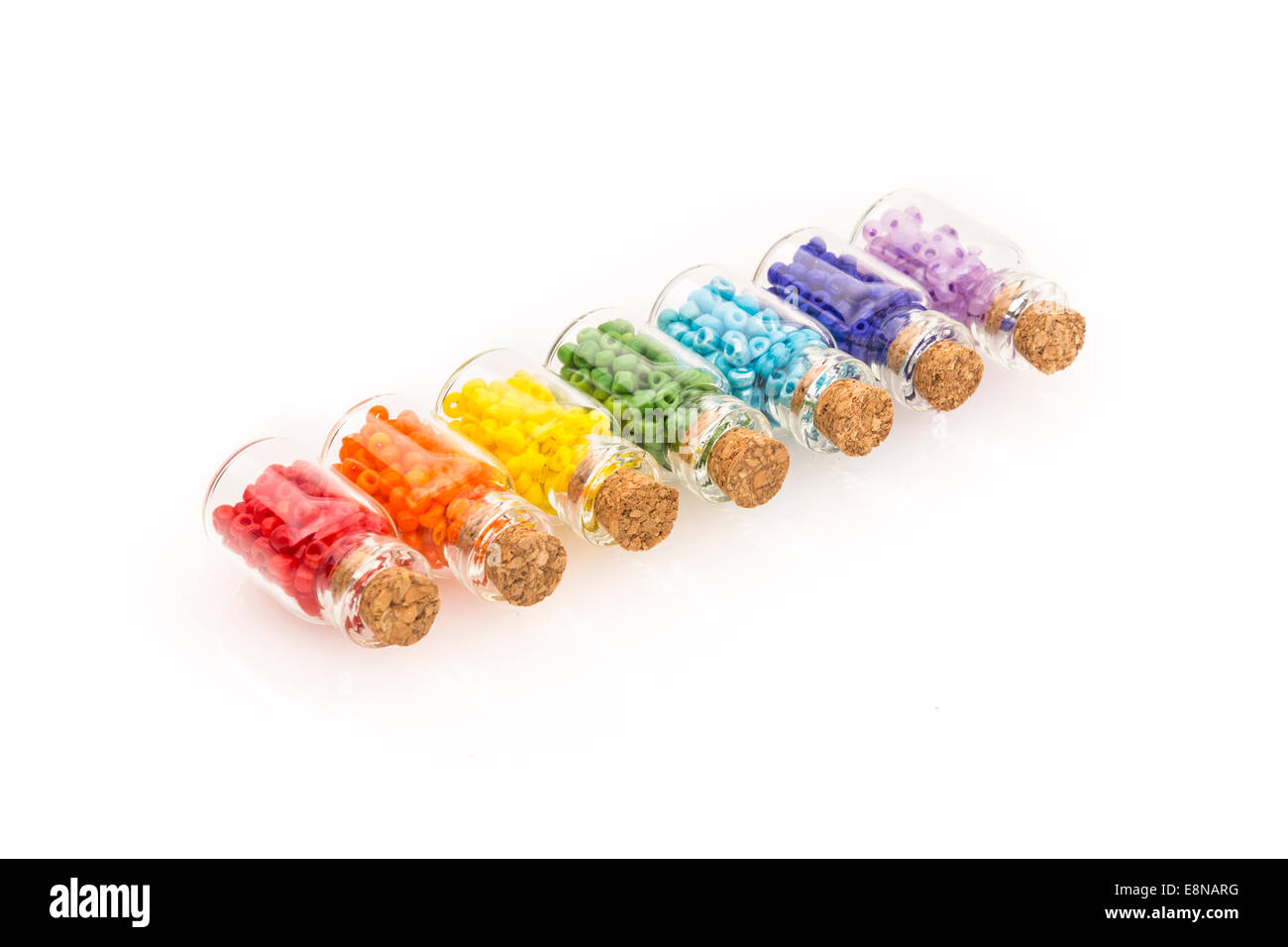 Petites bouteilles en verre avec un bouchon en liège, rempli d'un arc-en-ciel de couleurs de perles, sur un fond blanc Banque D'Images