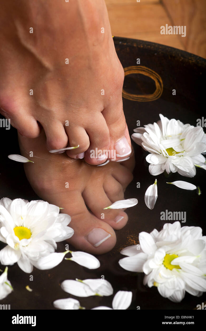 Pieds féminin dans un spa pour les pieds bol avec des fleurs Banque D'Images