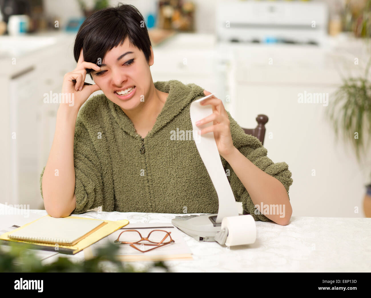 Jeune femme multi-ethnique tourmenter au sujet des calculs financiers dans sa cuisine. Banque D'Images