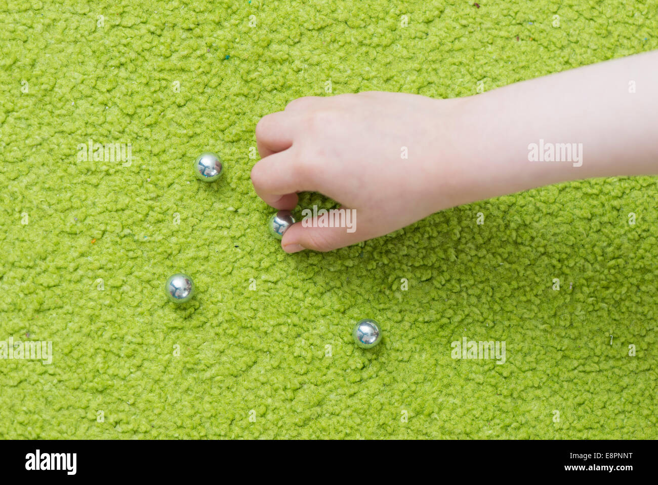 Main de l'enfant jouant avec des billes d'acier sur tapis vert. Banque D'Images