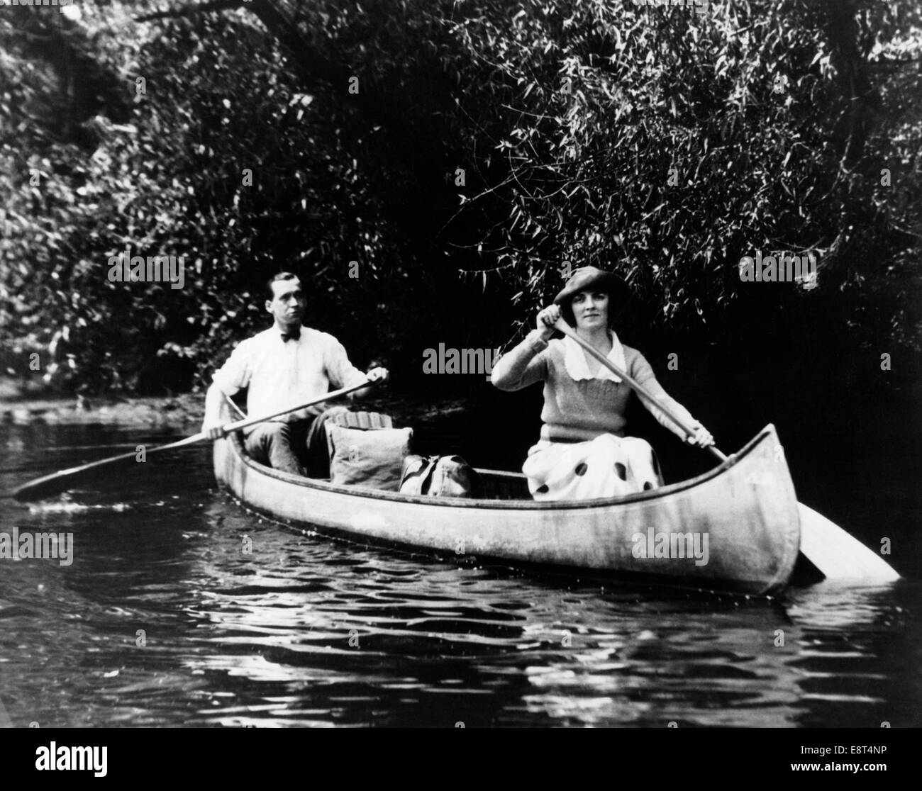 Années 1920 L'HOMME ET LA FEMME PADDLING CANOE DANS UN RUISSEAU LOOKING AT CAMERA Banque D'Images