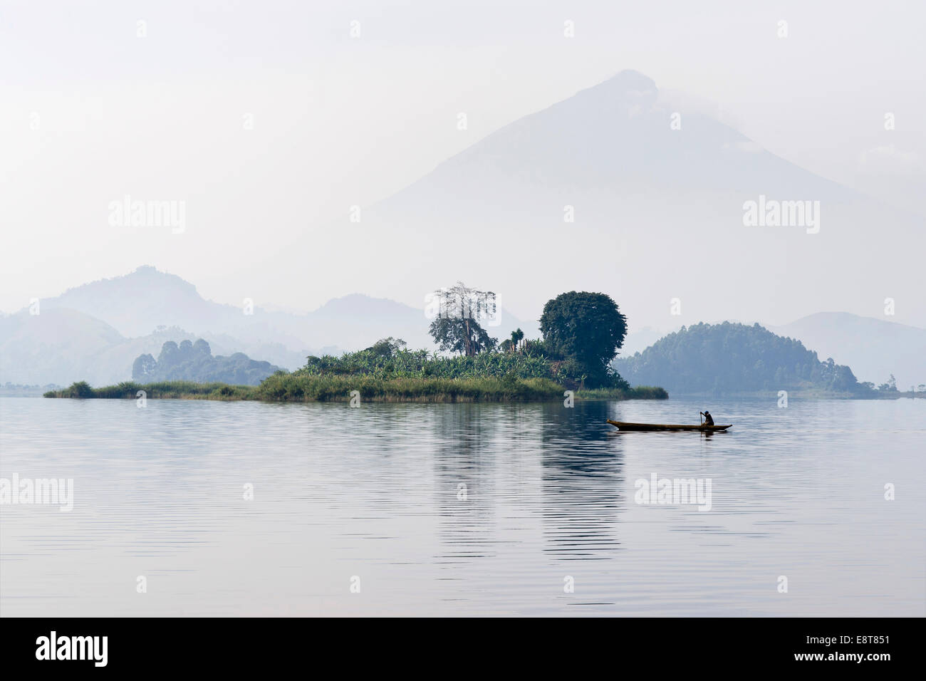 Canoe glisse dans la brume matinale sur le lac Mutanda en face du volcan Muhavura à la frontière avec le Rwanda, Kisoro Banque D'Images