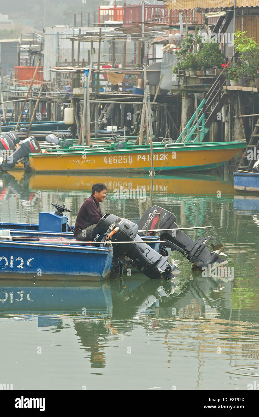 Pêcheur chinois 'Poisson' probablement parler, comme il est assis à l'arrière de son bateau de pêche sur la rivière à Tai O, Lantau Island, Hong Kong. Banque D'Images
