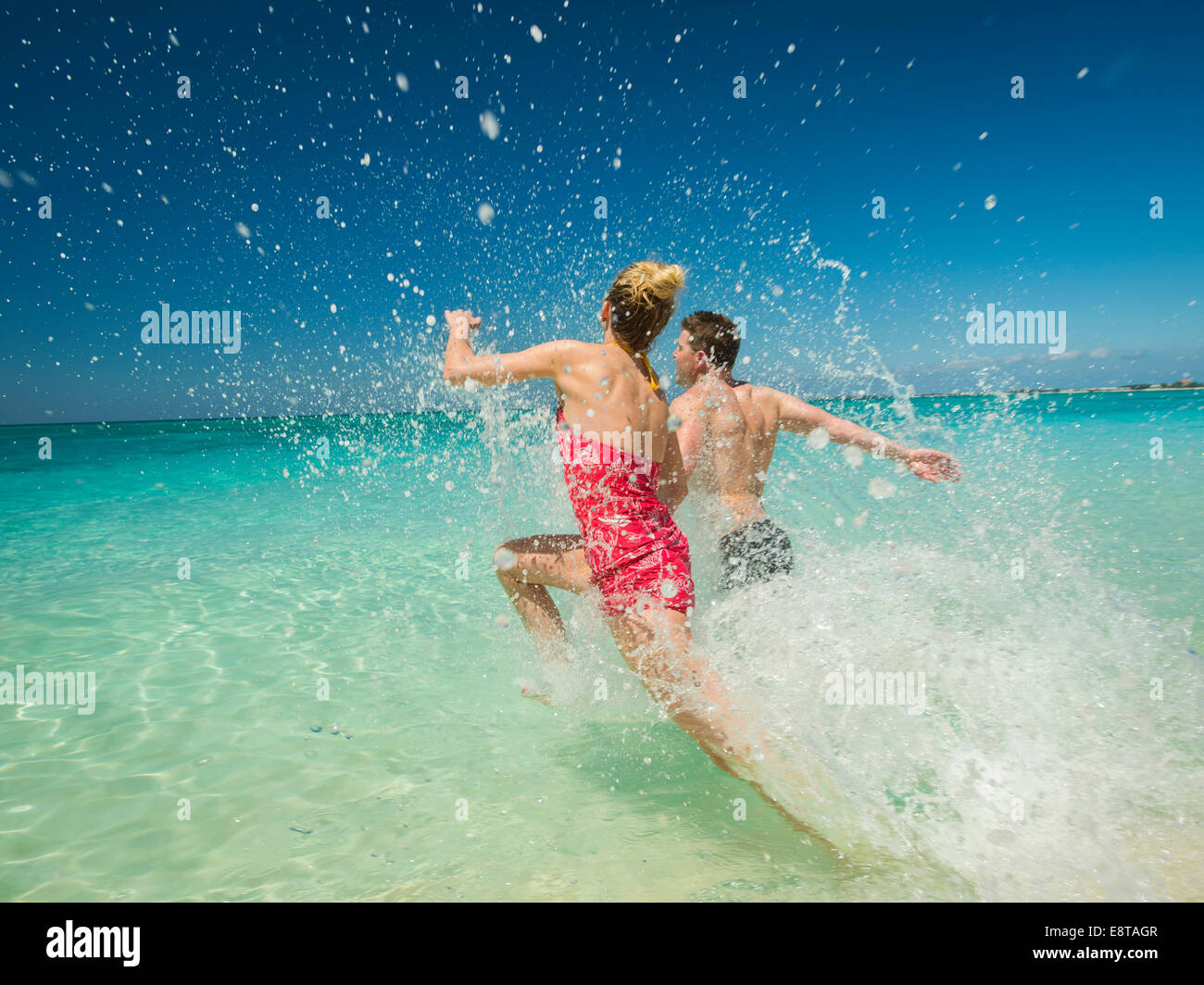 Couple s'éclabousser dans les vagues dans l'océan tropical Banque D'Images